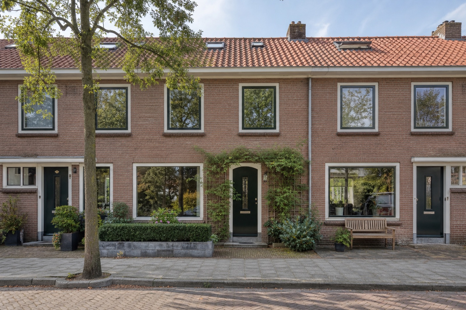 Rij bakstenen tussenwoningen met klimop rond een groene voordeur
