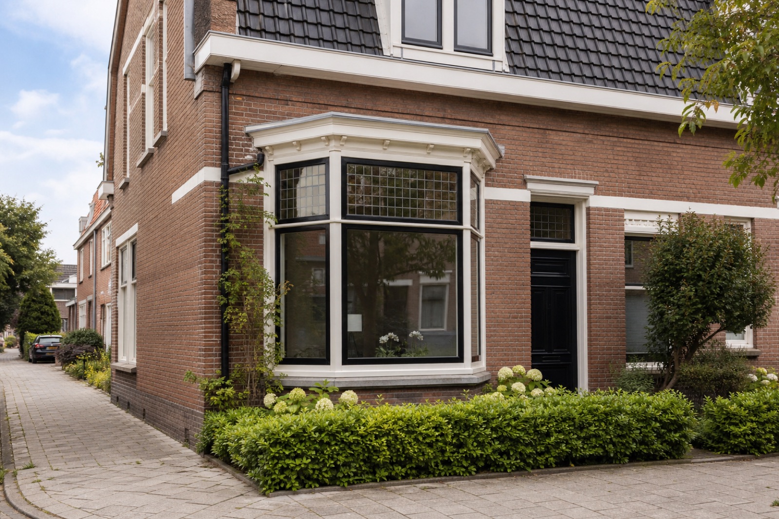 Hoekhuis van baksteen met erker en een voortuin met lage heg