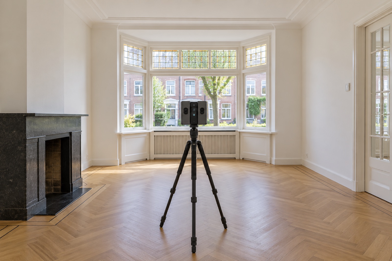 Lege woonkamer in een jaren-30-woning met erker, glas-in-lood en visgraatvloer, met een camera voor de virtuele tour op een statief