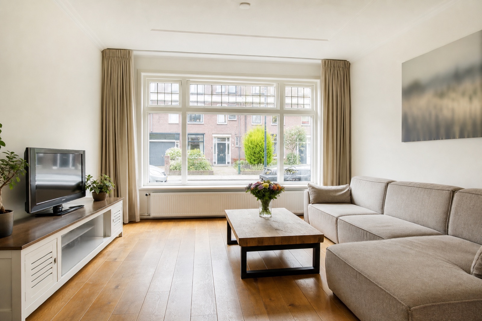 Lichte woonkamer met groot raam, bank en houten vloer