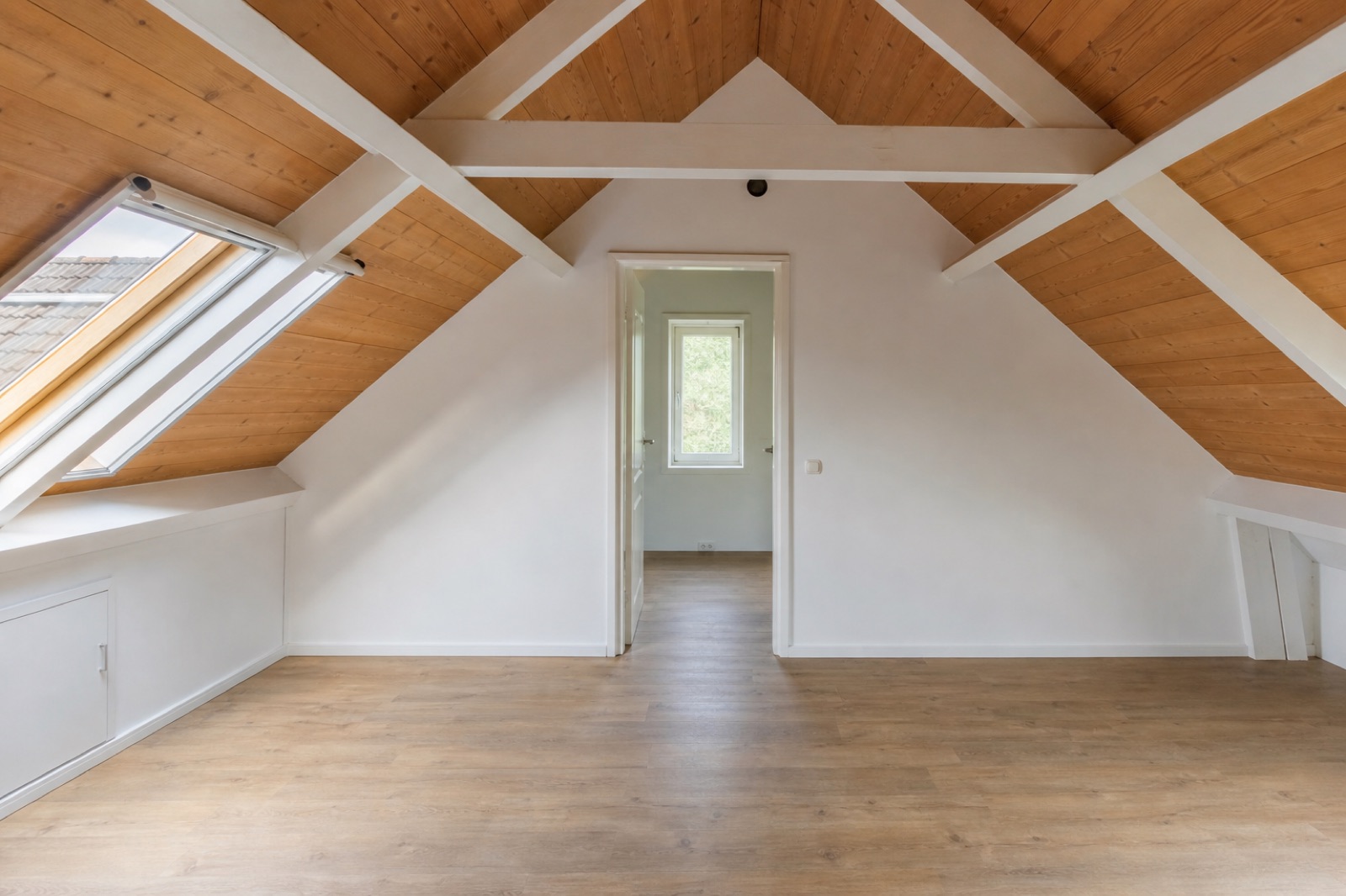 Lege zolder met een houten schuin dak, witte balken en een dakraam